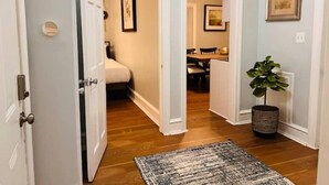 Un couloir doté d’un plancher en bois, d’un tapis, d’une plante en pot et d’œuvres d’art encadrées accrochées aux murs.