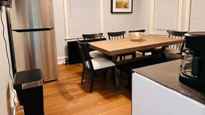 Une cuisine de taille réduite avec une table en bois, des chaises noires, un réfrigérateur en acier inoxydable et une machine à café.
