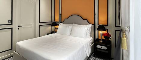 A neatly arranged bedroom with a large bed, a nightstand with a lamp, and patterned floor tiles.
