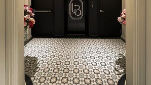 A hallway with a patterned floor, a black elevator with a logo, and a sign indicating an exit. - Le Bonheur Hotel (Phu Quoc)