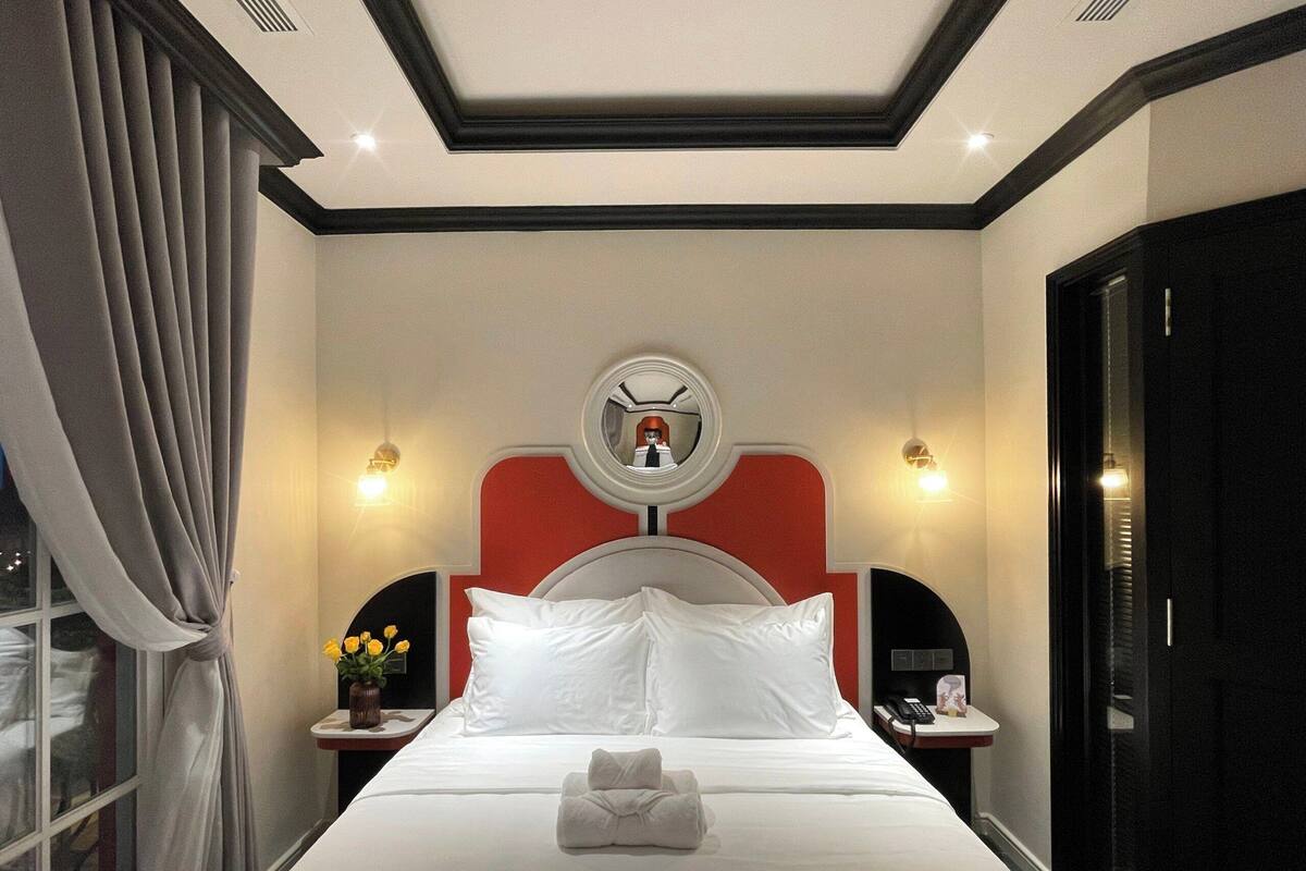A hotel room with a large bed, a round mirror above the headboard, bedside tables with lamps, and a window with curtains.