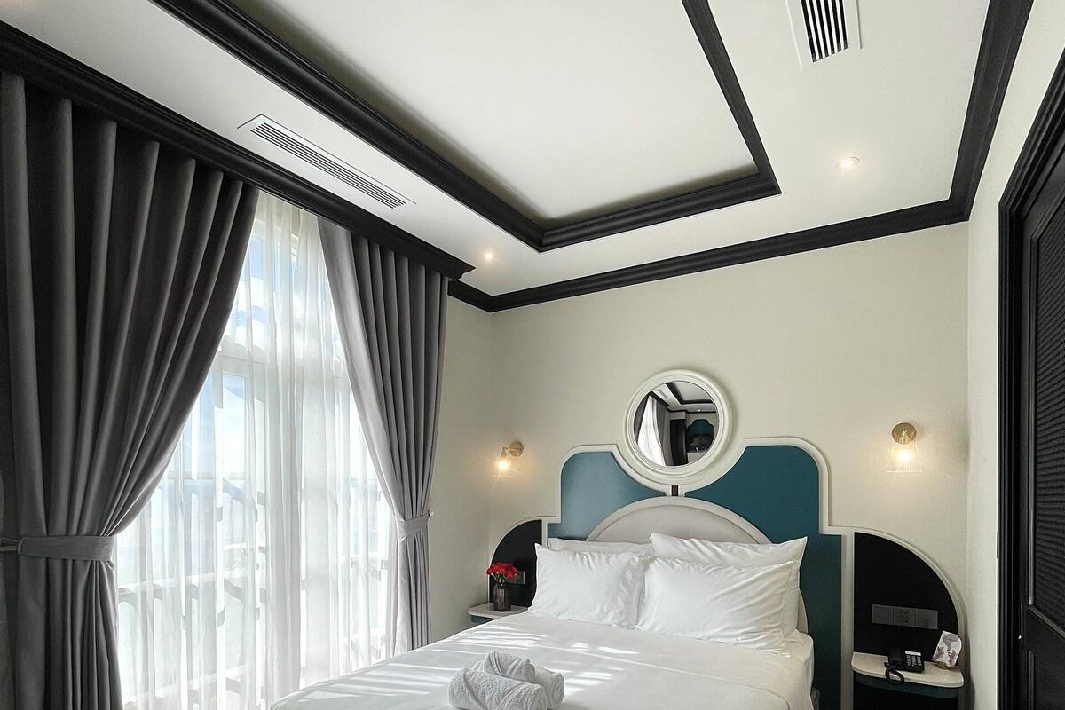 A modern hotel room with a large bed, a bedside table, a mirror, and a small desk with a chair.
