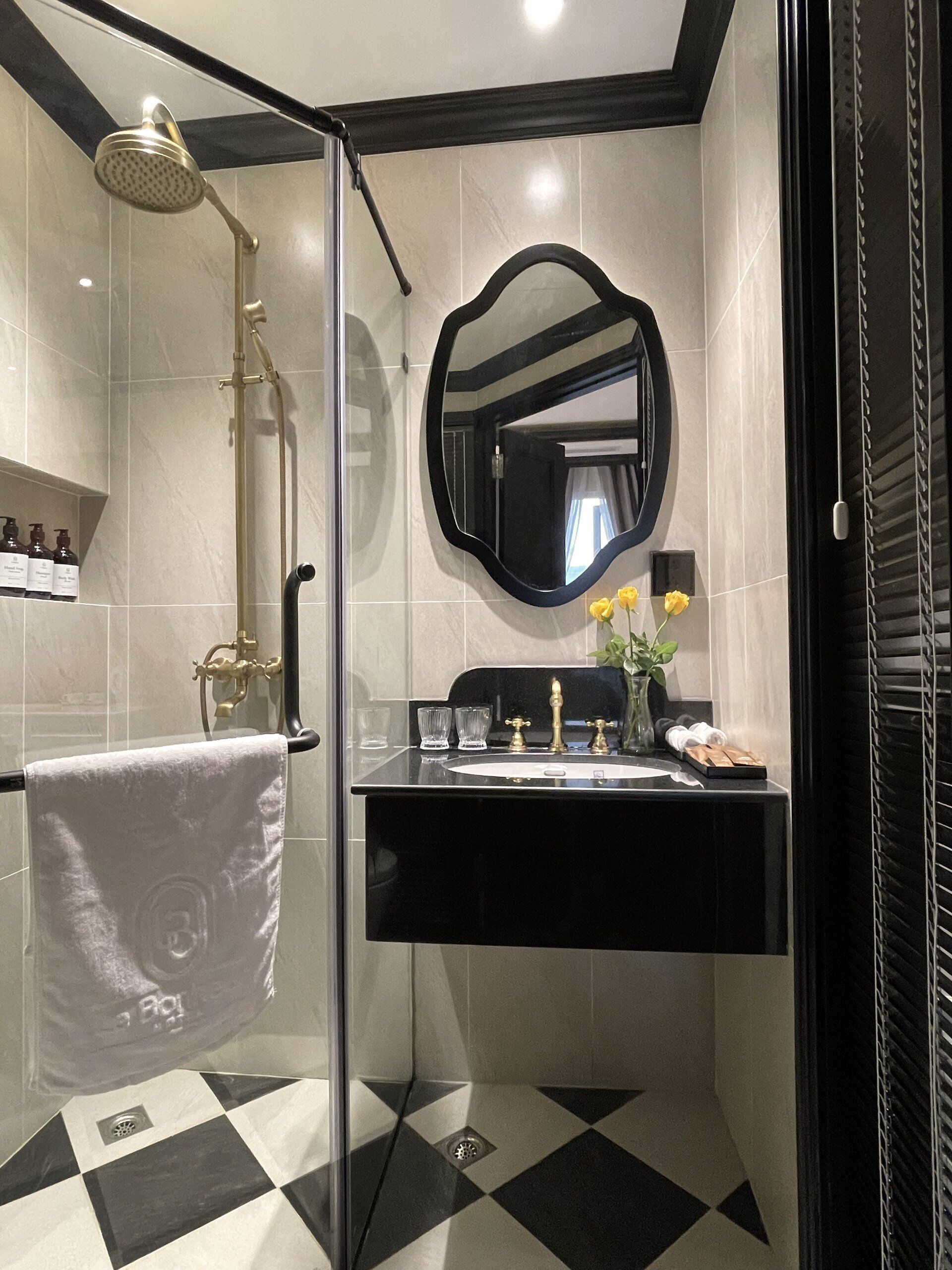A modern bathroom with a glass-enclosed shower, a black vanity with a gold faucet, and a large mirror.