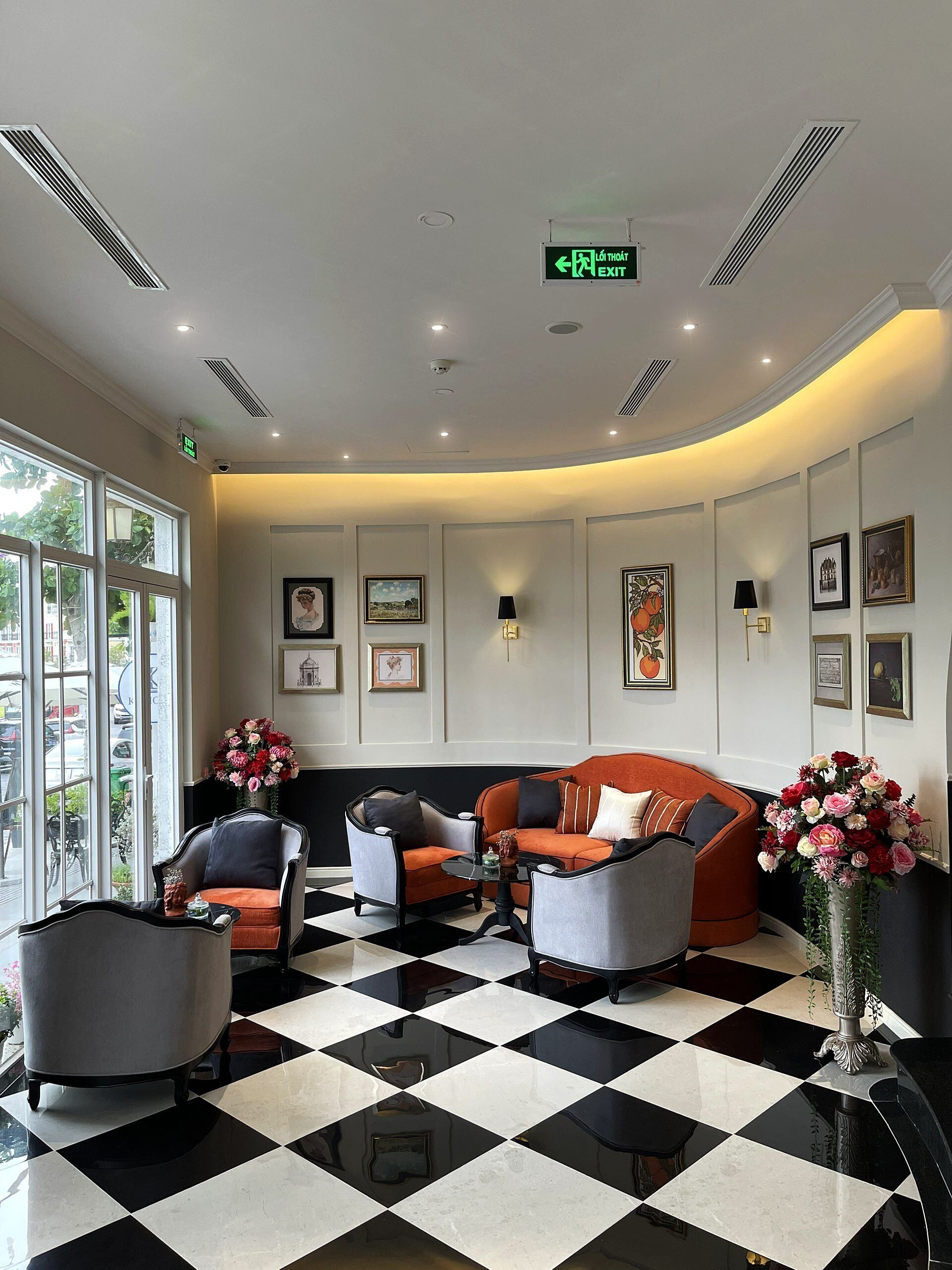 A lobby with a checkered floor, seating area with armchairs and a sofa, framed artwork on the walls, and a large window with a view of the outside.