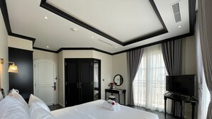 A hotel room with a large bed, a desk with a chair, a television, and a wardrobe. - Le Bonheur Hotel (Phu Quoc)