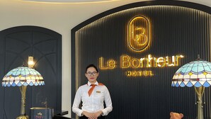 A hotel reception desk with a modern design, featuring a large illuminated sign, two decorative lamps, and a digital clock. - Le Bonheur Hotel (Phu Quoc)