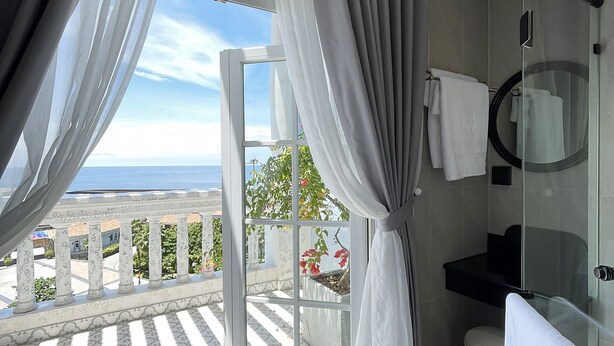 A modern bathroom with a glass shower, a white bathtub, and a view of the sea. - Le Bonheur Hotel (Phu Quoc)