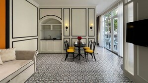 A modern hotel room with a dining area, a sofa, a TV, and a kitchen area. - Le Bonheur Hotel (Phu Quoc)