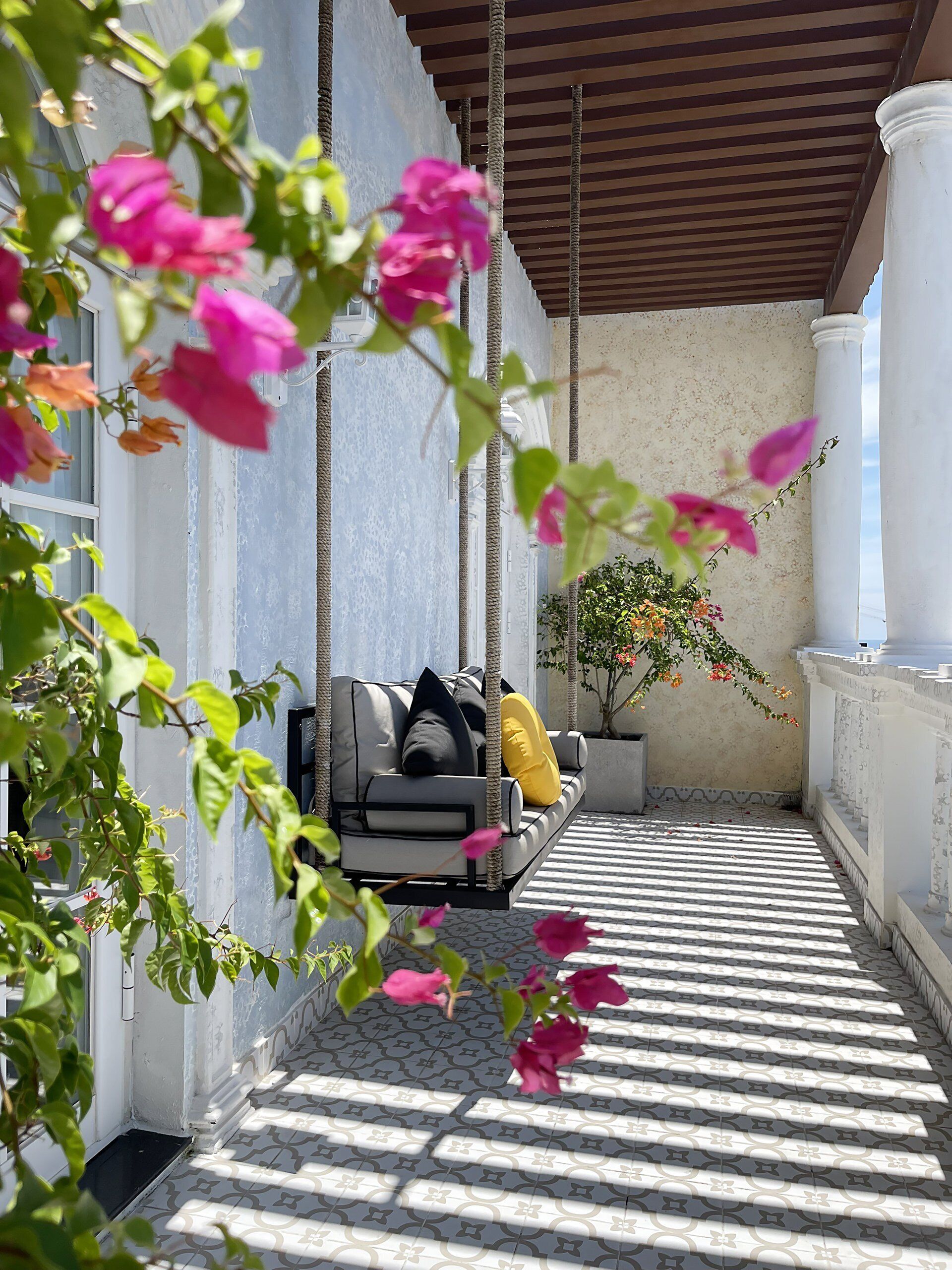A sunlit outdoor seating area with a sofa, a potted plant, and a patterned floor.