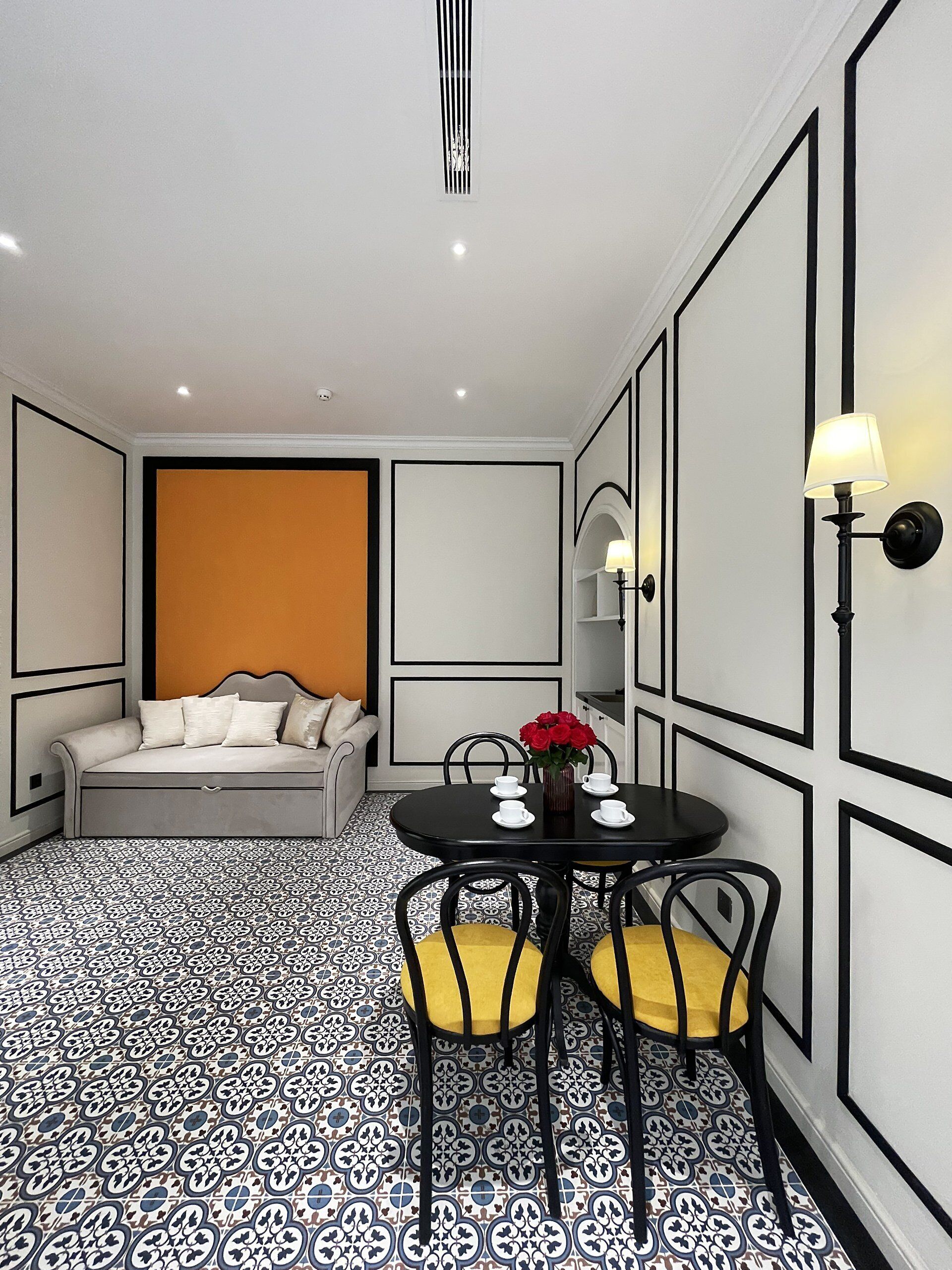 A room with a sofa, a dining table with chairs, and a vase with flowers.