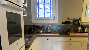 Een keuken met witte kasten, een ingebouwde oven, een raam met blauwe roede en een houten aanrecht.
