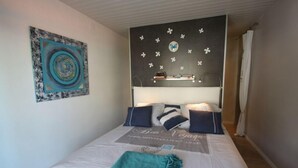 Een slaapkamer met een bed, kussens, een deken, een kunstwerk aan de muur en een plank met boeken.