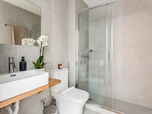 A modern bathroom with a white sink, a glass shower enclosure, and a toilet.