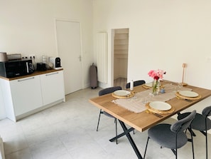 A modern kitchen with a microwave, toaster, and kettle. There is a dining table with plates, glasses, and a vase of flowers. - Town house (Marmande)