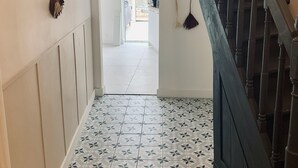 A hallway with patterned floor tiles, a staircase with dark balusters, and wall-mounted hooks with items.
