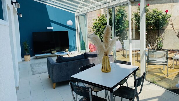 A modern outdoor living area with a glass enclosure, a sofa, a table, and a TV.