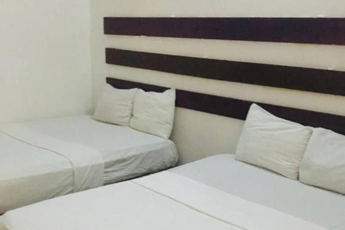 Une chambre d’hôtel avec deux lits simples et un lit plus grand, le tout équipé de linge de lit blanc.