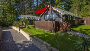 Una cabaña de madera con un toldo rojo, un porche con paredes de vidrio y un camino de ladrillo que lleva a la entrada.