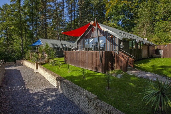 A wooden cabin with a red awning, a glass-enclosed porch, and a brick pathway leading to the entrance. - Luxury Self Catering Lodge with Hot Tub - Palms 2, Loch Etive, North Connel (North Connel)