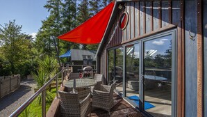 Un patio con mobiliario de mimbre, una parrilla y un ventanal que da a un espacio exterior.