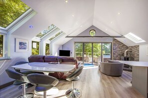 Ein geräumiges Loft mit hohen Decken, Oberlichtern, einem Essbereich, einem Kamin und einer großen Schiebeglastür, die auf eine Terrasse führt.
