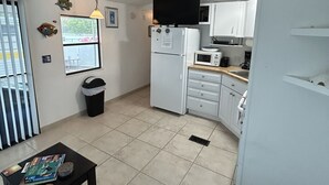 A compact kitchen with white cabinets, a microwave, and a refrigerator. There's a small dining area with a table and a chair. - Cozy Venture Out Cottage (Cudjoe Key)