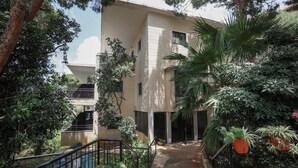 Un edificio moderno con un espacio exterior cubierto, rodeado de exuberante vegetación y plantas en macetas.