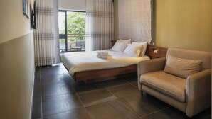 Una habitación de hotel con cama, sofá y balcón con cortinas.