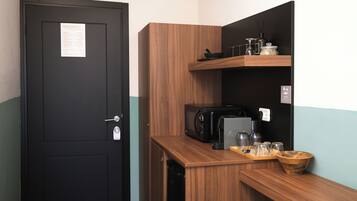 Una kitchenette compacta con microondas, cafetera y diferentes utensilios de cocina.