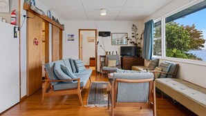 Een gezellige woonkamer met een bank, stoelen, een televisie en uitzicht op zee.