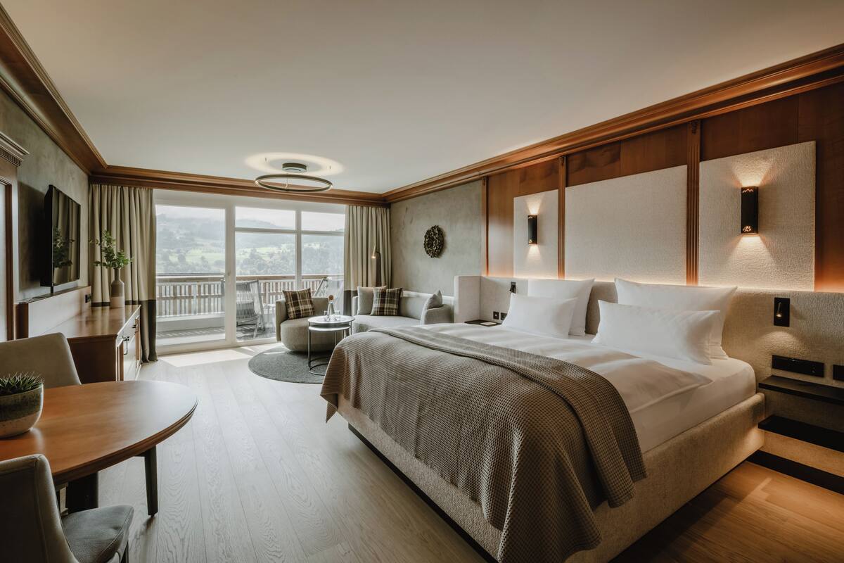 Habitació d'hotel moderna amb un llit gran, una zona de menjador, un balcó amb vistes i una televisió.