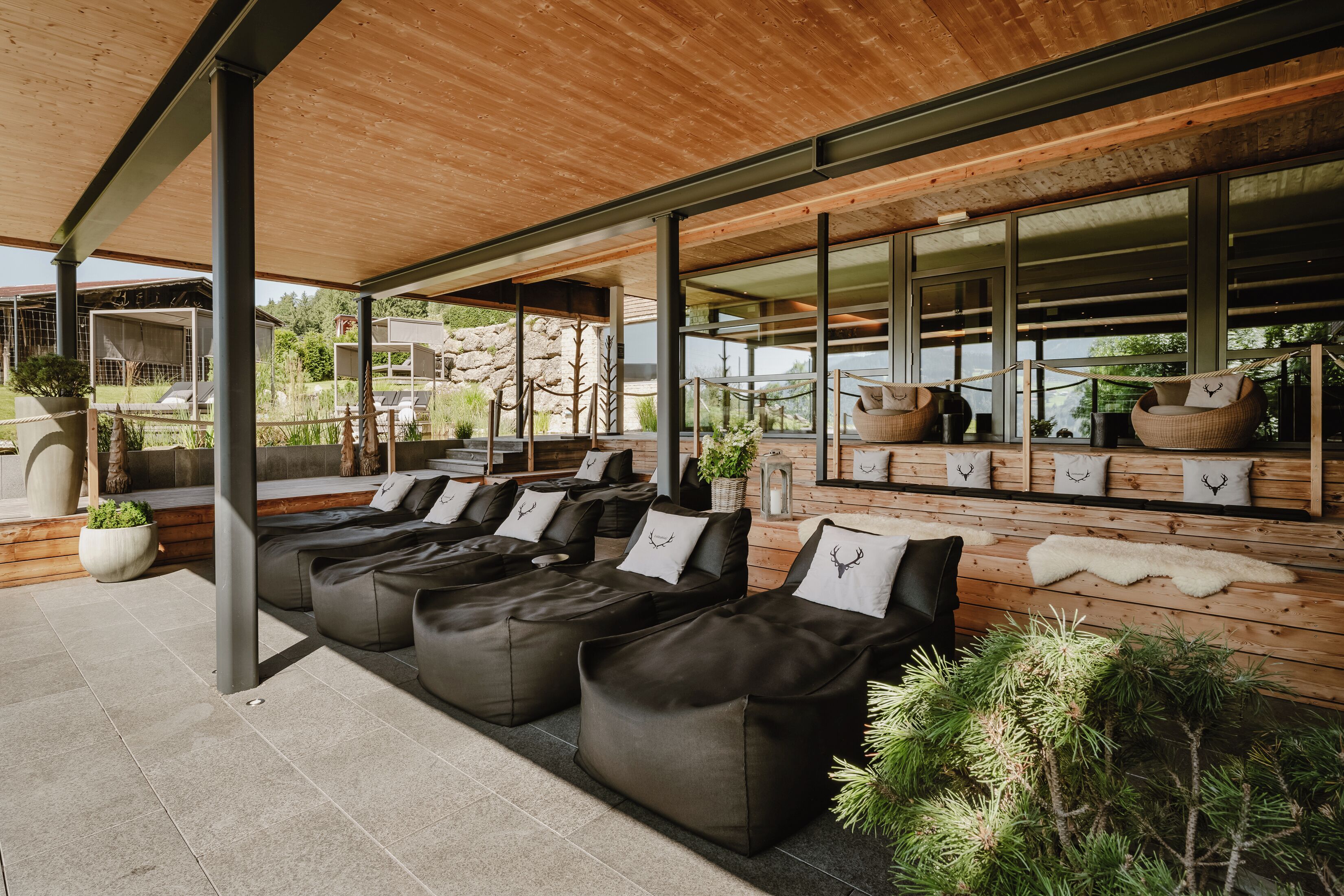 A modern outdoor lounge area with black cushioned seating and a wooden ceiling.