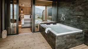Une salle de spa moderne dotée d’un grand jacuzzi, d’un plancher en bois et offrant une vue sur l’extérieur.