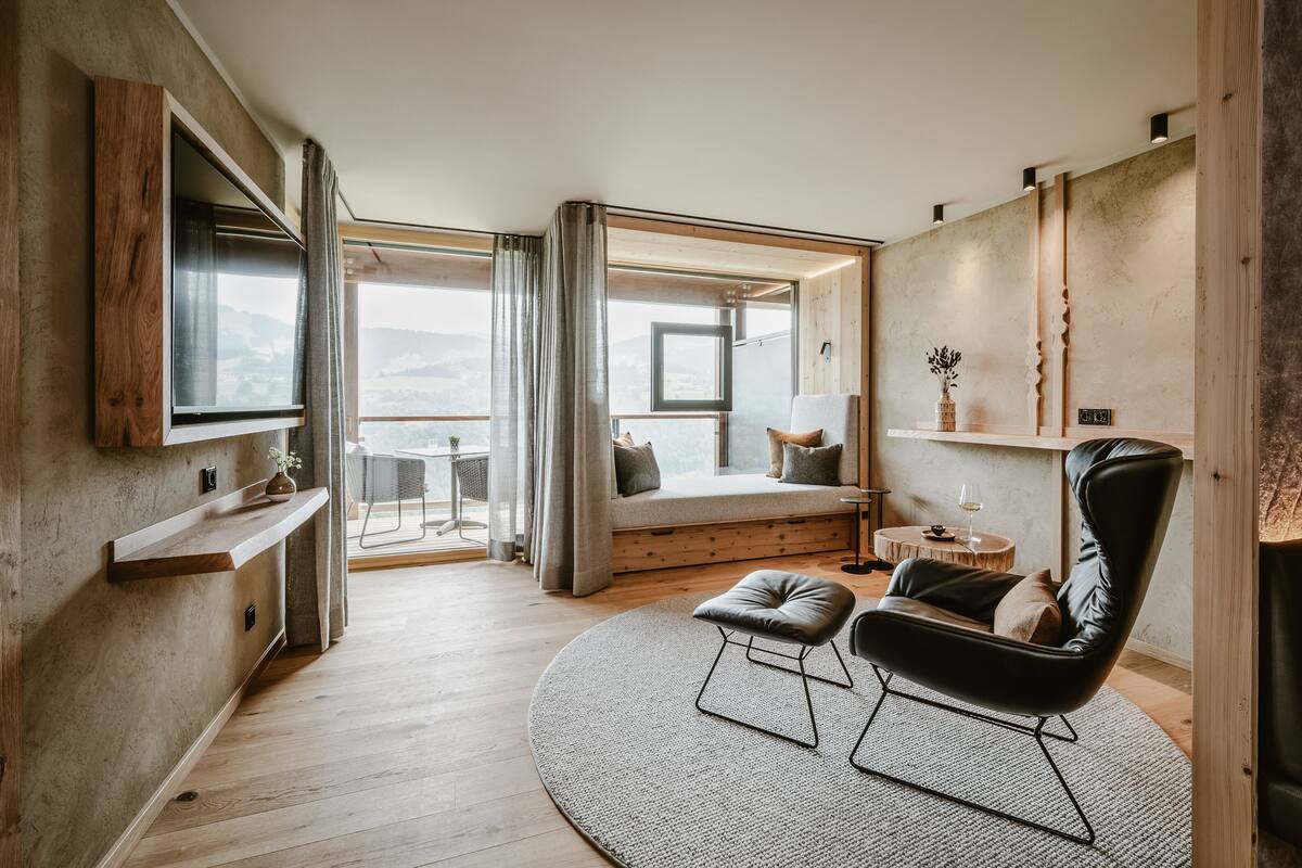 Habitació moderna amb una finestra gran, una cadira de cuir negre, un moqueta rodona i una prestatgeria de fusta.