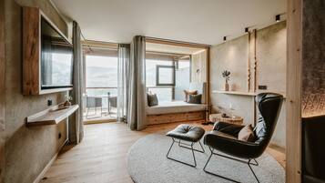 A modern room with a large window, a black leather chair, a round rug, and a wooden shelf.