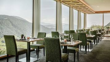 A restaurant with a mountain view, green upholstered chairs, and tables set for dining.
