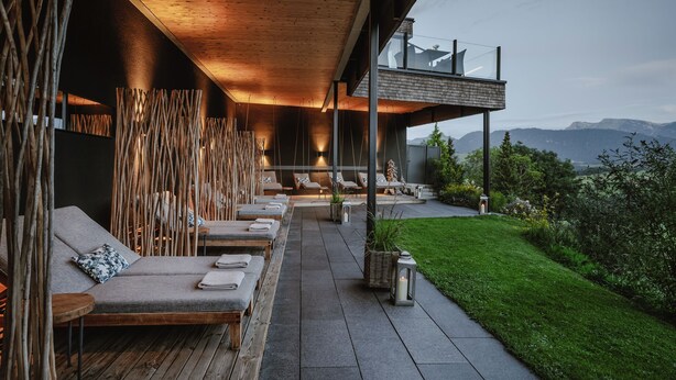 Un espace de détente extérieur moderne, doté de mobilier en bois et offrant une vue sur les montagnes.