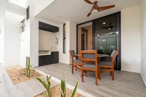 Een moderne eethoek buiten, met een houten tafel en stoelen, een plafondventilator en uitzicht door een glazen deur.