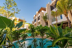 Een modern hotel met een zwembad, omringd door tropische planten.