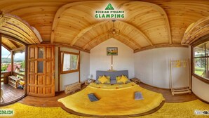 A room with a vaulted wooden ceiling, a bed with yellow bedding, a wooden door, and large windows offering a view of the outdoors.