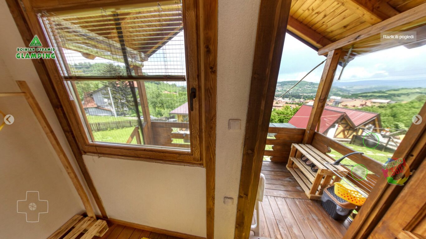A wooden balcony with a view of a rural landscape, a wooden bench, and a small table with items on it.