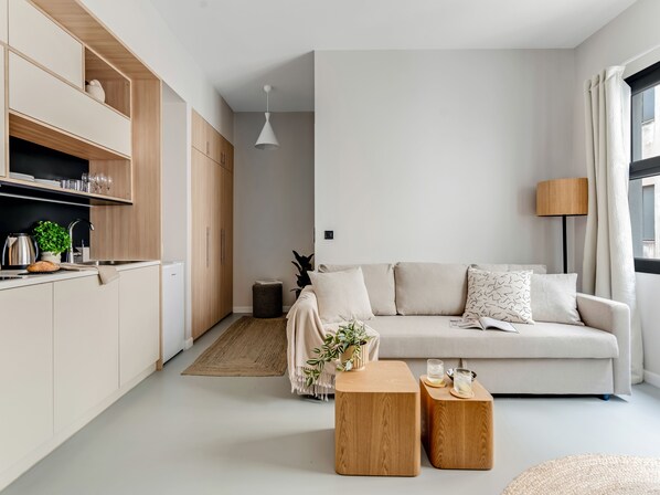 A modern, minimalist living space with a kitchen, a sofa, and two wooden side tables.
