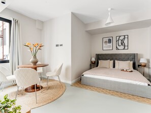 A modern bedroom with a bed, bedside tables, a round table with chairs, and a vase of flowers.