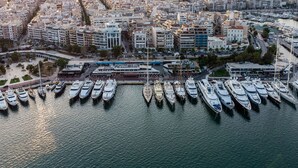 Eine Luftaufnahme einer Marina mit zahlreichen vertäuten Yachten, umgeben von dicht bebautem Stadtgebiet mit modernen Gebäuden und freiem Blick auf das Meer.