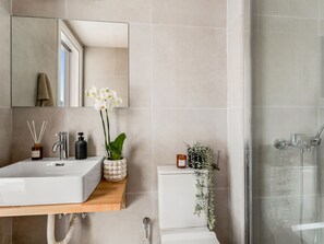 A modern bathroom with a large mirror, a white sink, a shower, and a toilet.