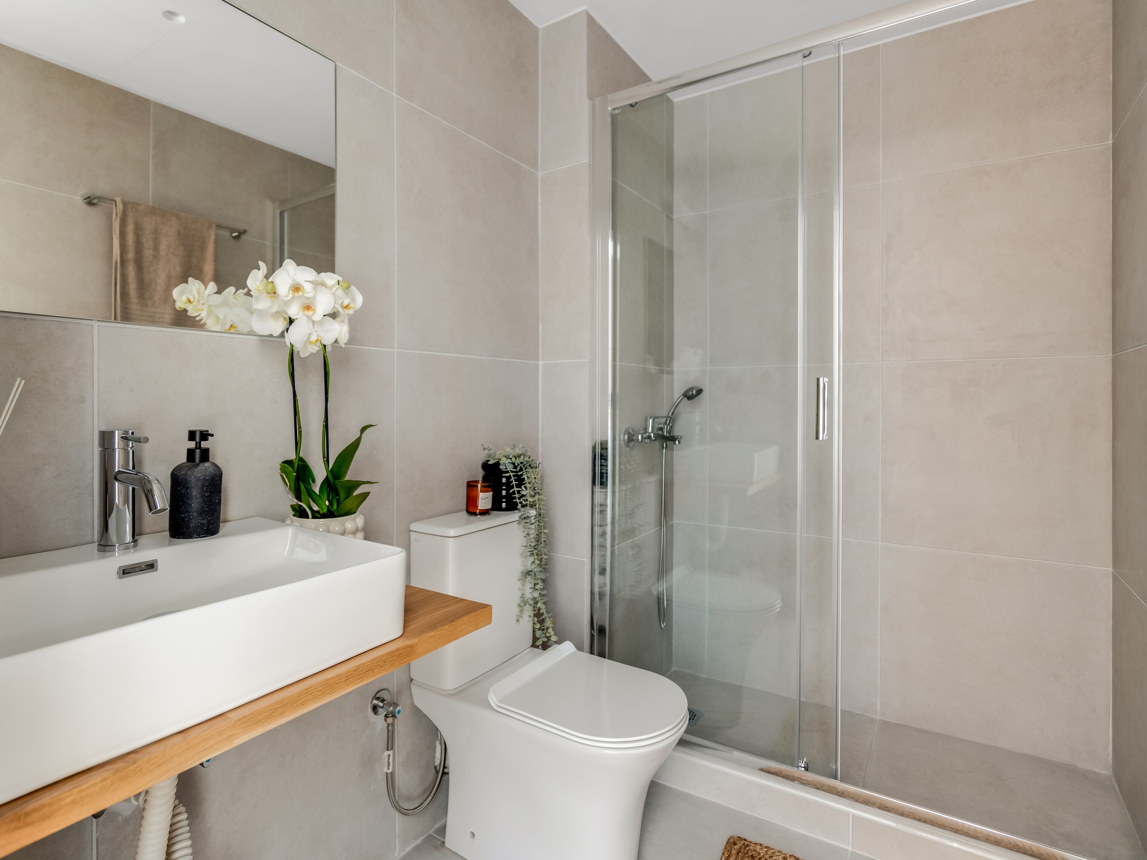 A modern bathroom with a glass-enclosed shower, a white sink with a wooden shelf, and a toilet.
