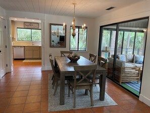A dining area with a wooden table, chairs, and a chandelier. There is a kitchen in the background with a dishwasher and cabinets. - 43 Woodbine Place at The Sea Pines Resort (Hilton Head Island)