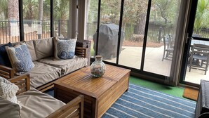 A spacious patio area with a wooden sofa, a coffee table, and a view of a covered grill and outdoor furniture. - 43 Woodbine Place at The Sea Pines Resort (Hilton Head Island)