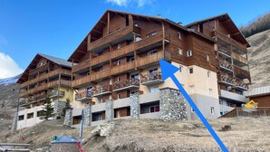Un edificio de madera de varios pisos con balcones, pilares de piedra y el cartel de un complejo de esquí.