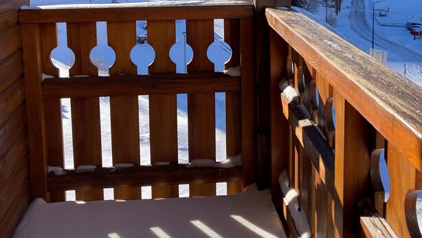 Un balcón de madera con vistas a una montaña nevada y edificios.